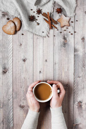Woman holding the cup of beverage. Wooden table decorated with christmas cookies