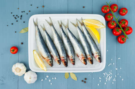 Raw fresh sardines in the white plate with ice and other ingredients on the blue wooden table, top viewの写真素材
