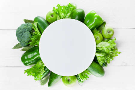 Empty plate with frame of green vegetables on the white wooden tableの写真素材