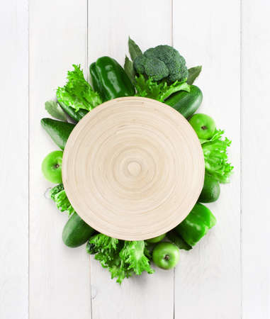 Empty plate with frame of green vegetables on the white wooden tableの写真素材