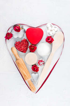 Heart of kitchen utensils, gift box and flowers on the textured white tableの写真素材