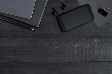 Black wooden table with smartphone and work accessories. Top view, copy space