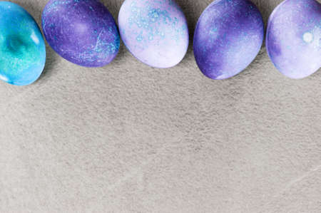 Gray textured background with blue and violet Easter eggs. Top view, copy spaceの写真素材