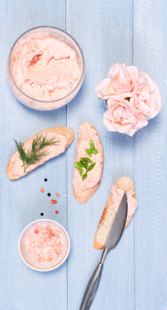 Homemade salmon pate in the glass jar and bread on blue wooden table, top view