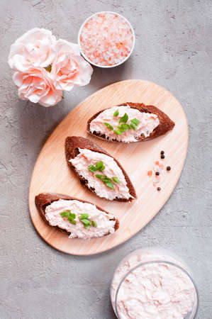 Salmon pate in the glass jar and on pieces of various bread on the cutting board. Top view.の写真素材