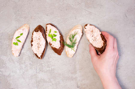 Female hand holding piece of rye bread with salmon pate, gray tableの写真素材