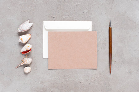 Blank craft postcard and envelope on the grey table with shells, top view