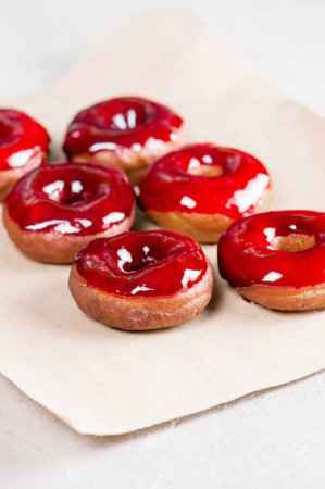 Fresh homemade donuts with red glaze on the sheet of craft paper, top viewの写真素材