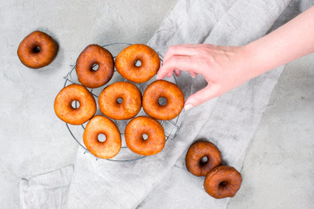 Female hand take fresh homemade donut, gray textured table, top view