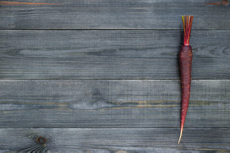 Violet carrot on the textured black wooden table, copy space