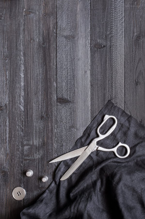 Black wooden sewing background with fabric and scissors, copy space