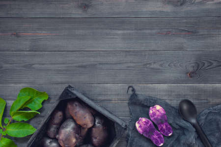 Black wooden background with fresh raw violet potatoes, copy spaceの写真素材
