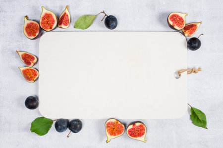 Background with white wooden cutting board decorated with fresh figs and plums, copy space