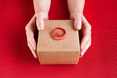 Female hands holding the decorated gift box, bright red backgroundの写真素材