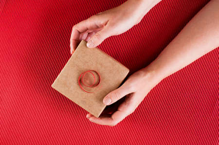 Female hands holding the gift box, bright red backgroundの写真素材