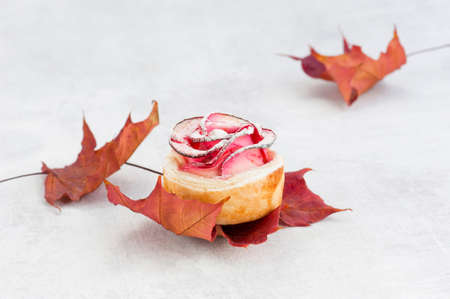 Beautiful apple rose cake coated with powdered sugar, composition with autumn leavesの写真素材