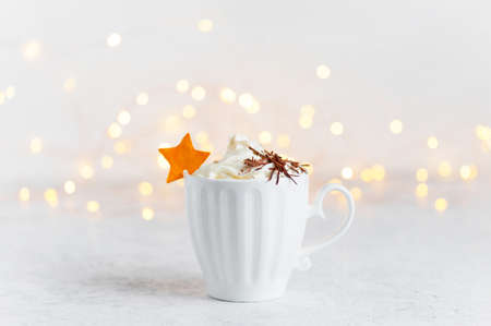 Cup of hot drink with whipped cream and chocolate decorated with citrus star, festive lights backgroundの写真素材