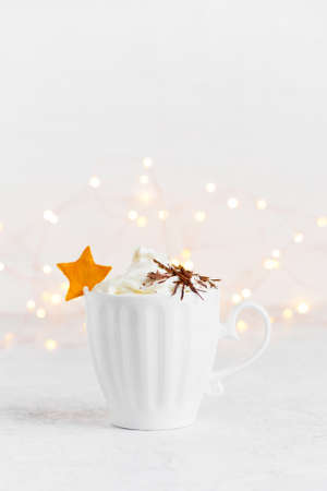 Cup of hot drink with whipped cream and chocolate decorated with citrus star, festive lights backgroundの写真素材