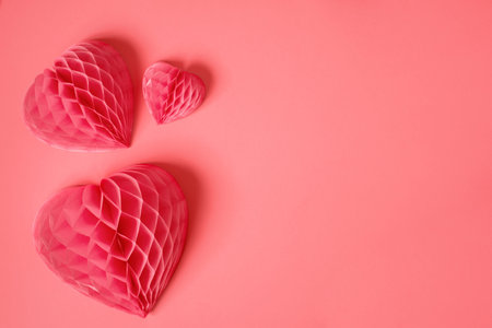 Coral-pink background with paper hearts, copy space
