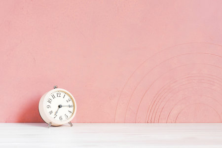 Alarm clock on the wooden white table against the pink-coral textured wall, copy spaceの写真素材