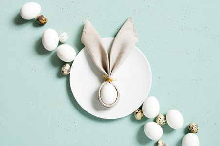 Chicken and quail eggs with bunny ears of linen napkin on the blue textured table, Easter...