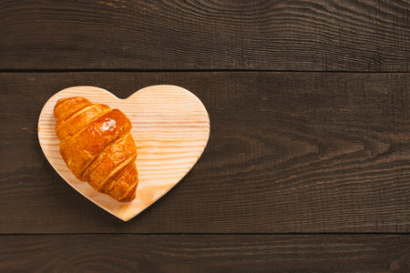 Fresh sweet croissant on the brown wooden table, top view