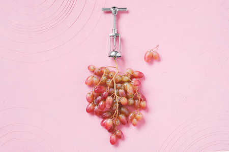 Natural wine production concept. Fresh ripe bunch of grapes with metal corkscrew on the textured pink table. Creative image, top viewの写真素材