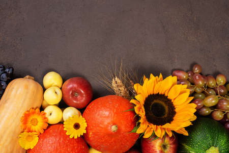 Brown textured background with fresh autumn fruits and vegetables, decorated with flowers. Background for autumn sale, organic market, harvest festival or thanksgiving day banners. Bright top view composition, copy spaceの写真素材