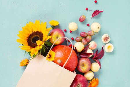 Craft paper bag with fresh autumn fruits and vegetables, decorated with flowers. Concept image for autumn sale, organic market, harvest festival or thanksgiving day. Bright top view composition, copy spaceの写真素材