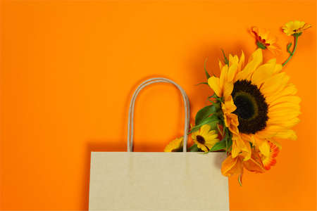 Craft paper bag with autumn bouquet with sunflower. Concept image for autumn sale, harvest festival or thanksgiving day. Bright top view composition, copy spaceの写真素材