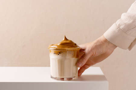 Female hand holding the glass of dalgona coffee, white tableの写真素材