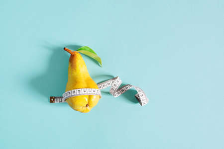 Weight loss concept, yellow pear checks body shapes with measuring tape, blue backgroundの写真素材