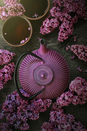 Teapot and two cups of tea on the dark wooden table decorated with blooming lilac, top viewの写真素材
