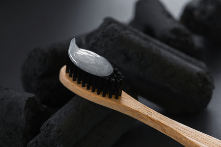 Bamboo toothbrush with charcoal bristles and toothpaste on the charcoal pieces, closeup