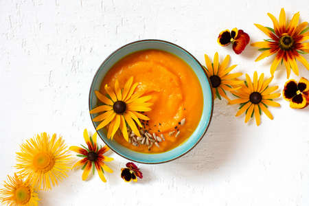 Pumpkin cream soup decorated with autumn flowers on the textured white table, top viewの写真素材