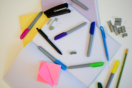 notebooks and pens with colored felt-tip pens and a stapler for studying at school on a white desk