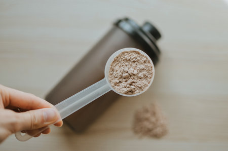 woman holding measuring cup with chocolate protein and shake nearby for making shake for athletesの写真素材