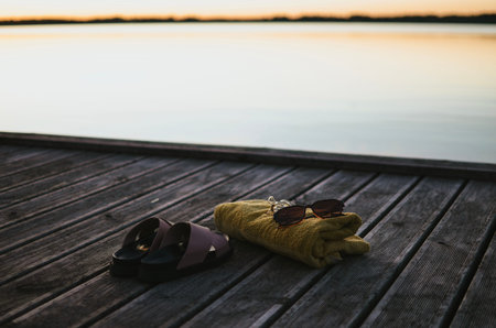 bathing towel, sunglasses and slippers against the backdrop of a lake on an evening sunny day for swimmingの写真素材