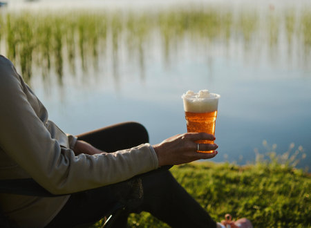 woman sitting and drinking light beer with foam by the lake at nice summer dayの写真素材