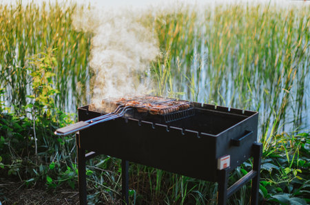 A young man is cooking juicy fish on a grill in nature on a lake in summer in Estoniaの写真素材