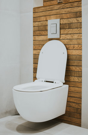white new toilet and metallic button mounted on the wall against a background of stylish wood tilesの写真素材