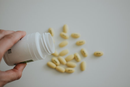 woman pours yellow pills from a jar on a white backgroundの写真素材