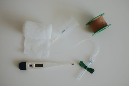 butterfly needle for drawing blood, thermometer, skin-colored tape and white bandage on a white...