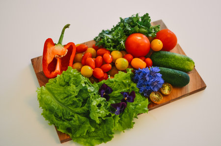 wooden board with vegetables like tomatoes, cucumbers, paprika and herbs on a white backgroundの写真素材