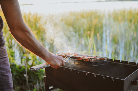 A young man is cooking juicy fish on a grill in nature on a lake in summer in Estoniaの写真素材