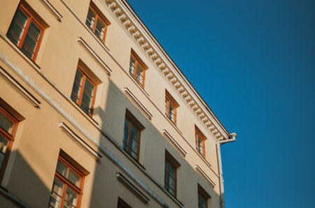an ancient yellow building with brown windows in the center of a European city on a sunny dayの写真素材
