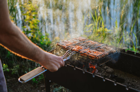 A young man is cooking juicy fish on a grill in nature on a lake in summerの写真素材