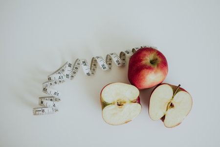 red full and cut in half apples and measuring tape on white backgroundの写真素材