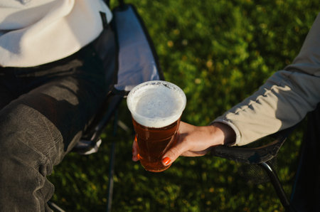 friends sitting and enjoying a summer evening and drinking light beer with foam by the lakeの写真素材