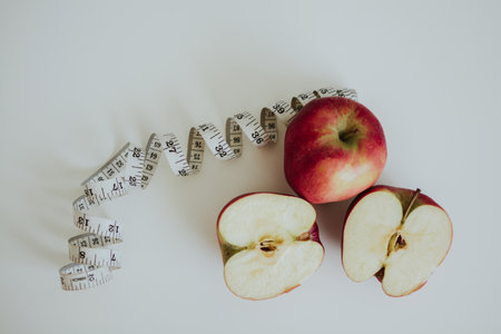 red full and cut in half apples and measuring tape on white backgroundの写真素材